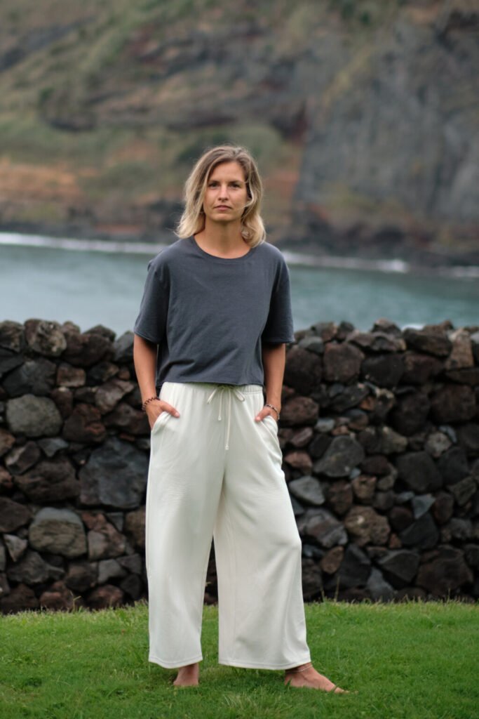 Captivating portrait of a young woman on São Miguel Island, framed by the stunning natural beauty of the Atlantic Ocean, vibrant green grass, and a striking black rock wall. The juxtaposition of the elements creates a visually compelling and harmonious composition.