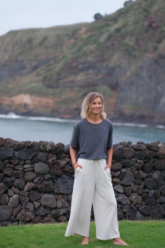 Captivating portrait of a young woman on São Miguel Island, framed by the stunning natural beauty of the Atlantic Ocean, vibrant green grass, and a striking black rock wall. The juxtaposition of the elements creates a visually compelling and harmonious composition.