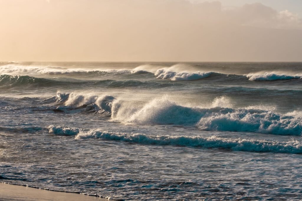 A breathtaking sunset over the beach, where gentle waves meet the shoreline, creating a serene and picturesque seascape. The warm hues of the setting sun cast a magical glow over the tranquil coastal scene